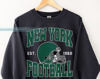 May include: Black sweatshirt with a green and white graphic of a football helmet and the text "NEW YORK FOOTBALL EST. 1960".