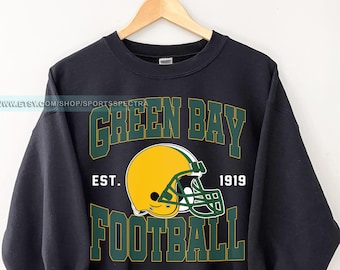 May include: Black sweatshirt with a green and yellow Green Bay Packers logo. The logo features a football helmet and the text "Green Bay", "Est. 1919", and "Football".