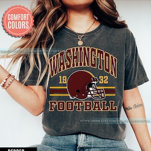 May include: A gray t-shirt with a vintage-style graphic of a football helmet and the text "WASHINGTON 19 32 FOOTBALL". The helmet is maroon and gold, and the text is in a distressed font.