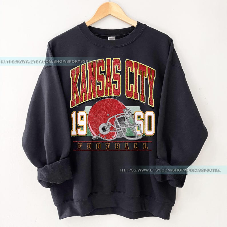 May include: Black sweatshirt with a vintage-style graphic of the Kansas City Chiefs logo, featuring a red helmet and the text "Kansas City 1960 Football".