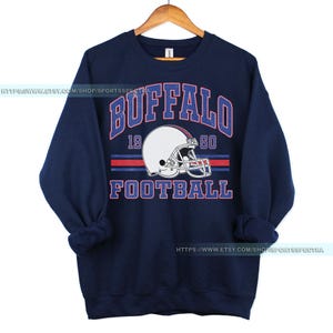 Może przedstawiać: Granatowa bluza z nadrukiem w stylu vintage przedstawiającym kask do futbolu amerykańskiego i tekst "Buffalo Football 19 60".