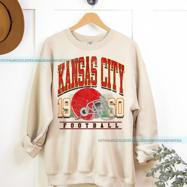 May include: A beige sweatshirt with a vintage-style graphic of a football helmet and the text "Kansas City 1960 Football".