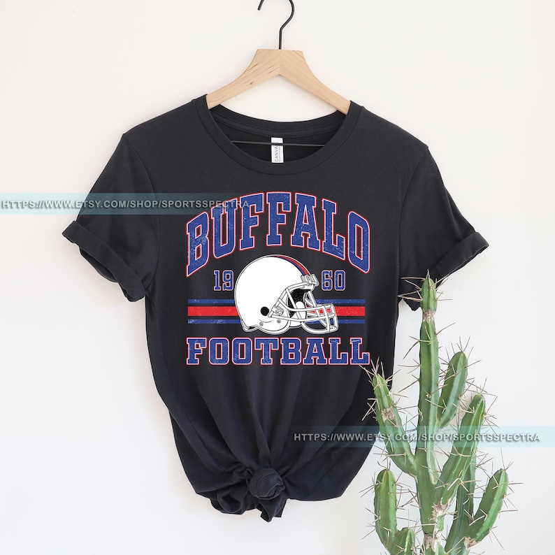 Może przedstawiać: Czarny T-shirt z grafiką w stylu vintage przedstawiającą kask do futbolu i tekst "Buffalo 19 60 Football".