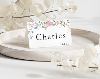 May include: White place card with a floral border in shades of pink and blue. The text "Charles" is printed in black, followed by "Table 3" in smaller font.