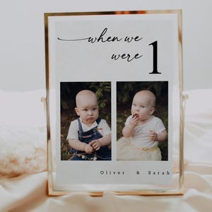 May include: A gold-framed photo display with the text "when we were 1" in black script. Two baby photos are below the text, with the names "Oliver & Sarah" at the bottom. The photos are of a baby in denim overalls and a baby in a white shirt and yellow skirt.