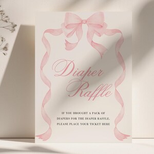 K&ouml;nnte beinhalten: Ein helles Schild mit dem Schriftzug "Diaper Raffle" in eleganter Schrift, umrahmt von einer rosa Schleife und B&auml;ndern im Aquarellstil. Der Text darunter lautet: "IF YOU BROUGHT A PACK OF DIAPERS FOR THE DIAPER RAFFLE. PLEASE PLACE YOUR TICKET HERE."