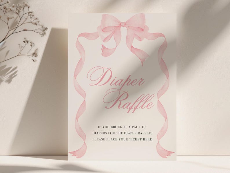 K&ouml;nnte beinhalten: Ein helles Schild mit dem Schriftzug "Diaper Raffle" in eleganter Schrift, umrahmt von einer rosa Schleife und B&auml;ndern im Aquarellstil. Der Text darunter lautet: "IF YOU BROUGHT A PACK OF DIAPERS FOR THE DIAPER RAFFLE. PLEASE PLACE YOUR TICKET HERE."