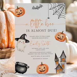 Op de afbeelding: Een Halloween-thema babyborrel uitnodiging met de tekst "a little boo is almost due!" in oranje script. De uitnodiging bevat illustraties van pompoenen, een spook met een heksenhoed, een vleermuis, een spinnenweb en een spookhuis. De uitnodiging is omringd door pompoenen.