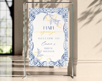 Op de afbeelding: Een welkomstbord voor een bruidsdouche, met een blauw-witte tegelrand. Het bord heeft een witte kern met blauwe en gele tekst, waaronder "Main Squeeze" en "Emma's Bridal Shower". Het ontwerp bevat citroenillustraties.