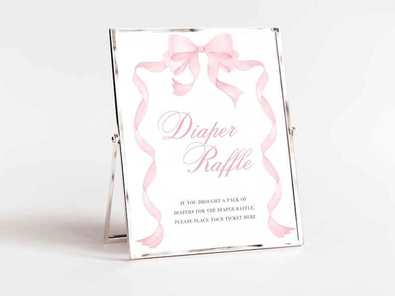 K&ouml;nnte beinhalten: Ein gerahmtes Schild mit den Worten "Diaper Raffle" in rosa Schrift, verziert mit einer Aquarellschleife und B&auml;ndern. Auf dem Schild steht: "Wenn Sie eine Packung Windeln f&uuml;r die Windel-Tombola mitgebracht haben, legen Sie bitte Ihr Ticket hier ab."