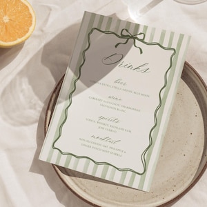 Pode incluir: Um cartão de menu de bebidas com um padrão de listras verdes e brancas, adornado com uma borda verde e um laço. Apresenta uma lista de cervejas, vinhos, destilados e coquetéis. Colocado em um prato bege, com frutas cítricas ao fundo.