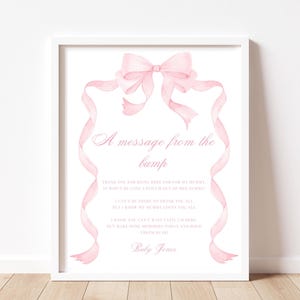 Può includere: Una stampa incorniciata con bordo bianco presenta un design ad acquerello. Un fiocco rosa e nastri incorniciano il testo "A message from the bump" e una poesia. La stampa è su sfondo bianco ed è firmata "Baby Jones".