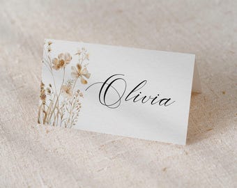 May include: A white place card with a floral design in shades of brown and beige. The name "Olivia" is written in black cursive script.