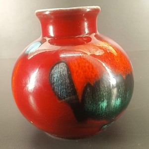 Könnte beinhalten: Eine kleine, runde, rote Keramikvase mit schwarzen und grünen abstrakten Mustern. Die Vase hat eine glänzende Oberfläche.