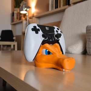 May include: An orange dragon-shaped controller holder with blue eyes, holding a white and black video game controller. The controller has a plus-shaped directional pad and black control sticks.