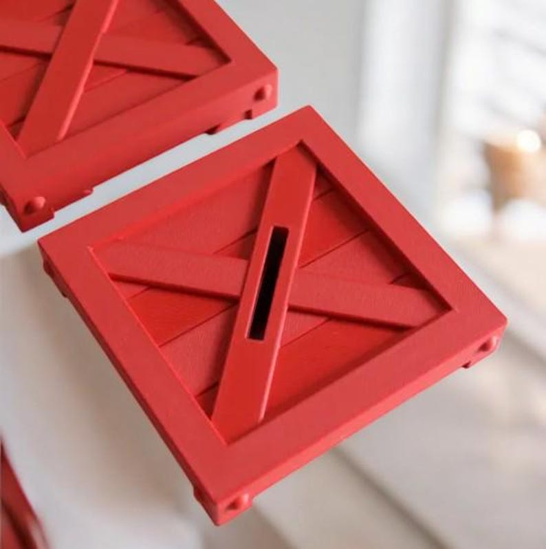 May include: Two red wooden money boxes with a crate design. Each box has a square shape with a slot for inserting money. The boxes have a rustic, farmhouse style.