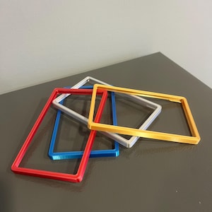 May include: A collection of rectangular frames in red, blue, silver, and yellow. The frames are stacked and slightly overlapping, showcasing their vibrant colors and simple design. The frames appear to be made of plastic or a similar material.