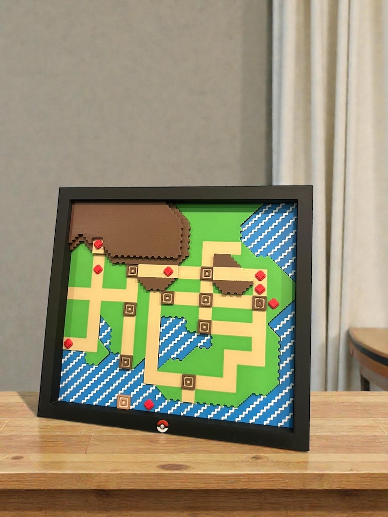 May include: Framed map art featuring a pixelated design with green, brown, and blue elements. The map is set against a black frame and includes red accents. A Pok&eacute; Ball is visible at the bottom.