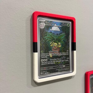 Puede incluir: Una tarjeta coleccionable de Pok&eacute;mon enmarcada con Exeggutor. El marco es rojo, negro y blanco, montado en una pared gris. La tarjeta muestra una colorida ilustraci&oacute;n de Exeggutor en un entorno selv&aacute;tico, con texto que detalla sus habilidades.