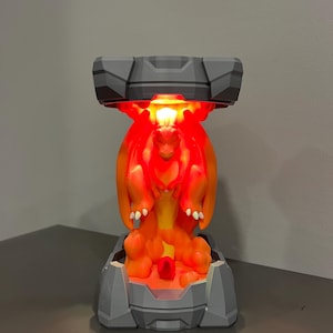 May include: A gray and orange lamp featuring a dragon design. The lamp has a gray base and top, with an orange dragon figure in the center. The dragon is illuminated with a red glow.