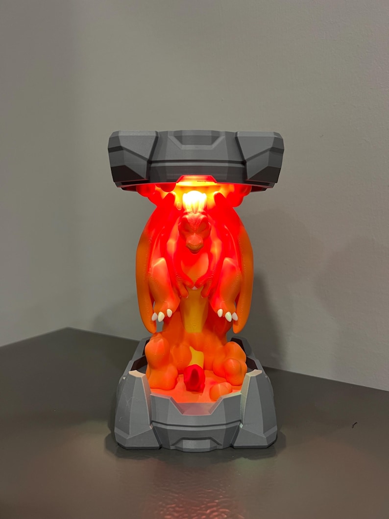May include: A gray and orange lamp featuring a dragon design. The lamp has a gray base and top, with an orange dragon figure in the center. The dragon is illuminated with a red glow.