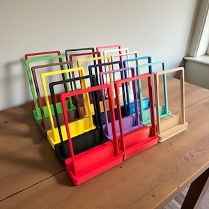 May include: A collection of colorful, rectangular organizers with a handle and a tray base. The organizers are in various colors, including red, yellow, black, green, and blue. They are arranged on a wooden table.