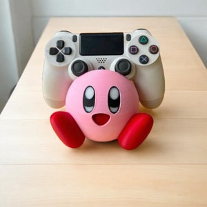 May include: A pink and red 3D printed character holding a white PlayStation 4 controller. The character has large eyes and a wide smile.