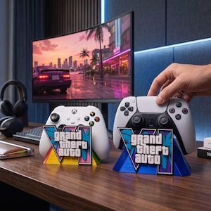 Op de afbeelding: Twee gamecontroller-standaards met het Grand Theft Auto VI-logo. De gele standaard houdt een witte Xbox-controller vast, terwijl de blauwe standaard een witte PlayStation 5-controller ondersteunt. Beide standaards tonen de speltitel.