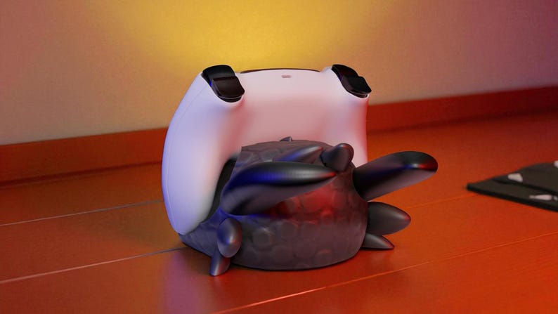 May include: A white and black gaming controller rests on top of a dark gray, textured object with rounded edges and protruding shapes. The controller has black accents and is positioned on a reddish-orange surface.