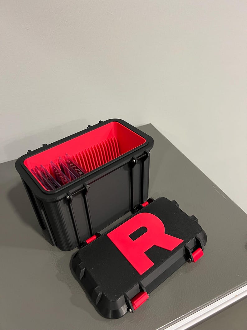 K&ouml;nnte beinhalten: Schwarze rechteckige Aufbewahrungsbox mit rotem Innenraum und passendem Deckel. Der Deckel hat ein gro&szlig;es rotes "R" und rote Verschl&uuml;sse. Die offene Box zeigt einen roten Innenraum mit vertikalen Trennw&auml;nden.
