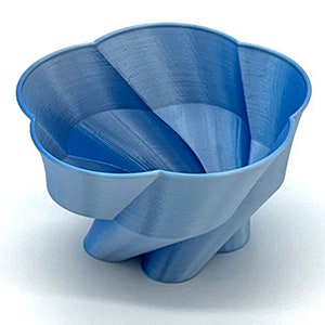 May include: A light blue ceramic bowl with a unique, swirling, and geometric design. The bowl has a wide, open top and a narrow base.
