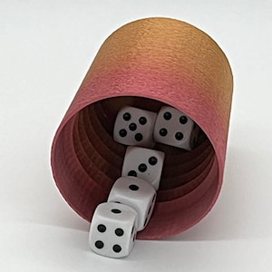 May include: A pink and orange dice cup with white dice spilling out. The dice have black dots on each side.