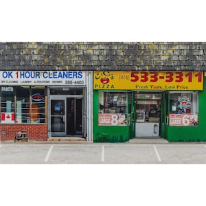 May include: Exterior shot of two adjacent storefronts. The left one is "OK 1 Hour Cleaners" with a Canadian flag. The right one is a pizza shop, "CC's Pizza", with a yellow sign and the phone number (416) 533-3311. Both have open doors.