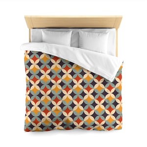 May include: A bed with a light wood headboard and white pillows. The duvet cover features a repeating geometric pattern of overlapping circles in shades of orange, yellow, teal, and dark purple. The bed is made and ready for use.