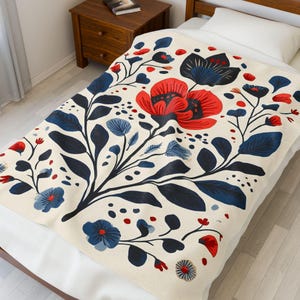 May include: A cream-colored blanket with a floral pattern. The design features large red and blue flowers, dark blue leaves, and smaller blue and red floral accents. The blanket is spread across a bed.
