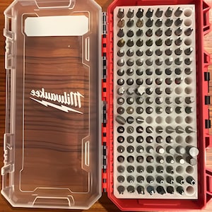 May include: A red and clear plastic case with a Milwaukee logo on the side. The case contains a variety of different sized and shaped screwdriver bits.