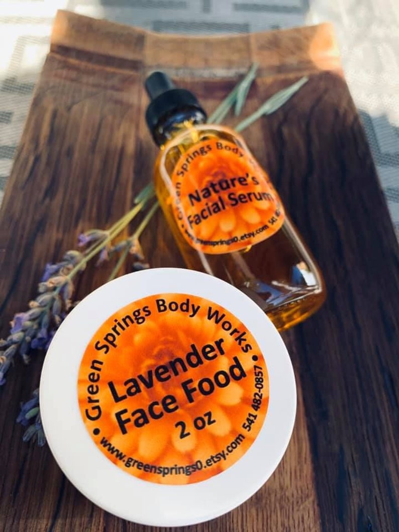May include: A white jar with a yellow and orange label that reads "Green Springs Body Works Lavender Face Food 2 oz www.greensprings0.etsy.com 541 482-0857". A clear glass bottle with a dropper and a yellow and orange label that reads "Green Springs Body Nature's Facial Serum greensprings0.etsy.com" is next to the jar.
