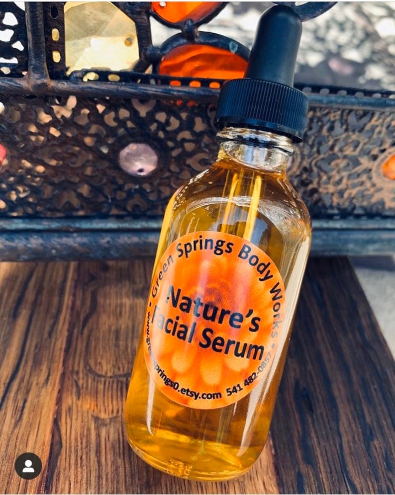 May include: A clear glass bottle with a black dropper top filled with a yellow liquid. The bottle has a round orange label that reads "Green Springs Body Works - Nature's Facial Serum - greensprings0.etsy.com 541 482-0857".