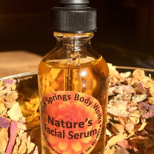 May include: A clear glass bottle with a black dropper top filled with a yellow liquid. The bottle has a round label with the text "Nature's Facial Serum" and the website address "greensprings0.etsy.com".