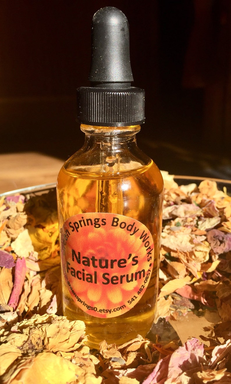 May include: A clear glass bottle with a black dropper top filled with a yellow liquid. The bottle has a round label with the text "Nature's Facial Serum" and the website address "greensprings0.etsy.com".