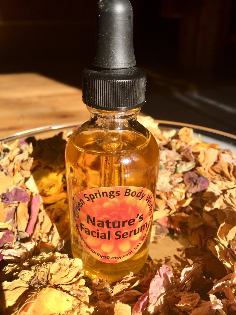 May include: A clear glass bottle with a black dropper top filled with a yellow liquid. The bottle has a label that reads "Green Springs Body Works Nature's Facial Serum greensprings0.etsy.com". The bottle is sitting on a bed of dried flower petals.