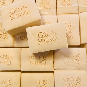 May include: A collection of rectangular, off-white soap bars. Each bar is stamped with the words "GREEN SPRINGS" in a sans-serif font. The bars are arranged in a close-up, overhead shot, suggesting a bulk product.