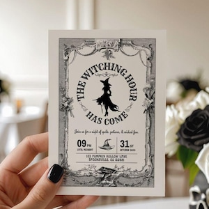 Op de afbeelding: Een Halloween-uitnodigingskaart met de tekst "The Witching Hour Has Come" in een decoratieve lijst. De kaart toont een silhouet van een heks en evenementdetails. De kaart wordt voor een bloemstuk gehouden.
