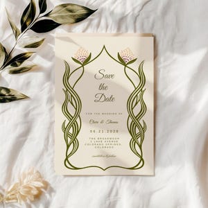 Plain, bright white, sheet background with shadows a sprig of an olive branch that as been dried - it gives boho, nature vibe without too much clutter. There is a small white flower in the corner. In the center of the mock up is an art nouveau  save the date card. The card's border are garden green vines, and a hand illustrated wildflower at the top.