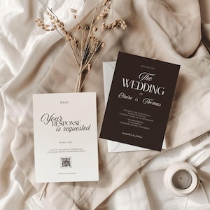 以下が含まれることがあります： 結婚式の招待状セット。メインの招待状は濃い茶色で、白文字で「The Wedding of Claire & Thomas」と書かれています。 「Your response is requested」というテキストの RSVP カードも含まれています。 セットはニュートラルな生地の上に置かれています。
