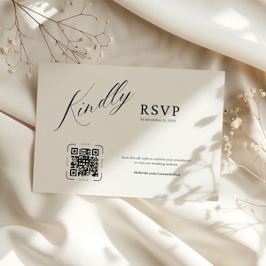Może przedstawiać: Kremowa karta RSVP z czarnym napisem "Kindly" i "RSVP by December 31, 2025." Zawiera kod QR i adres strony internetowej. Karta jest umieszczona na miękkiej, białej tkaninie z delikatnymi dekoracjami kwiatowymi.