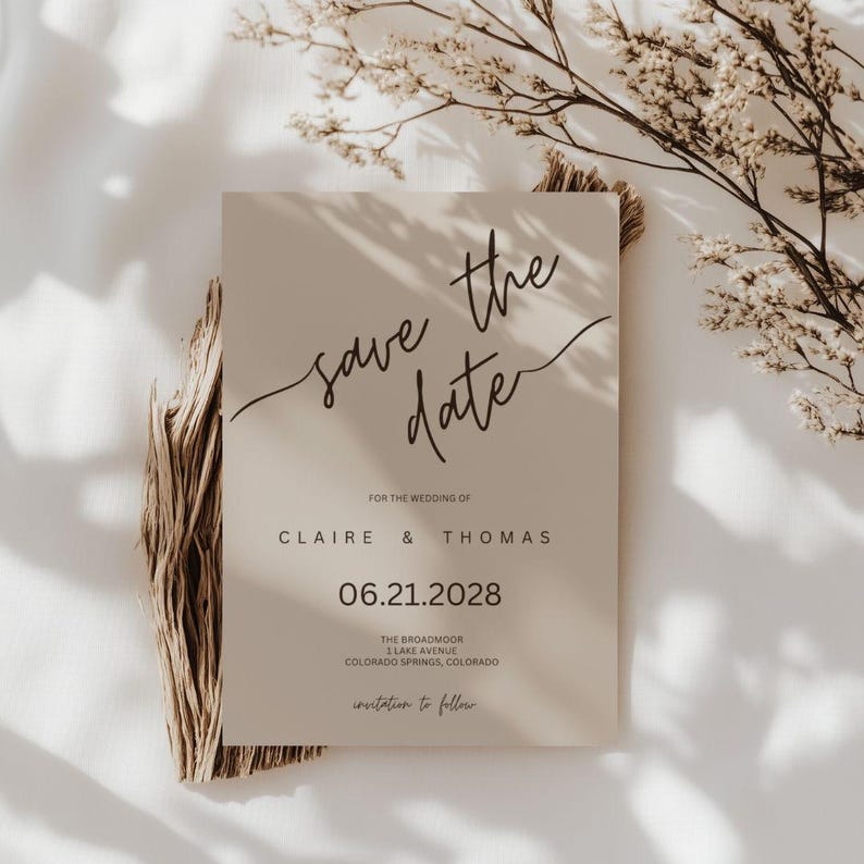 This is a lifestyle mockup photo with a white linen background, there is a sprig of dried willow branches on the edge of the mockup. In the center of the mockup is an example of the save the date card.