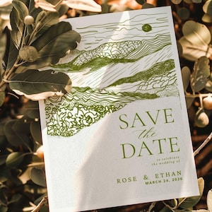 May include: A white card with green line art of a landscape and the words "SAVE the DATE" in elegant script. The card also includes the names "ROSE & ETHAN" and the date "MARCH 24, 2026".