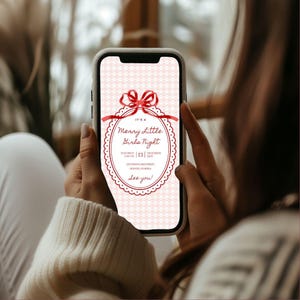 This is a lifestyle image of a women holding a phone - the background is blurred out but represents a Winter window. On the phone screen is a Christmas party invitation for a girls night in.