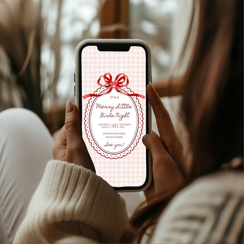 This is a lifestyle image of a women holding a phone - the background is blurred out but represents a Winter window. On the phone screen is a Christmas party invitation for a girls night in.